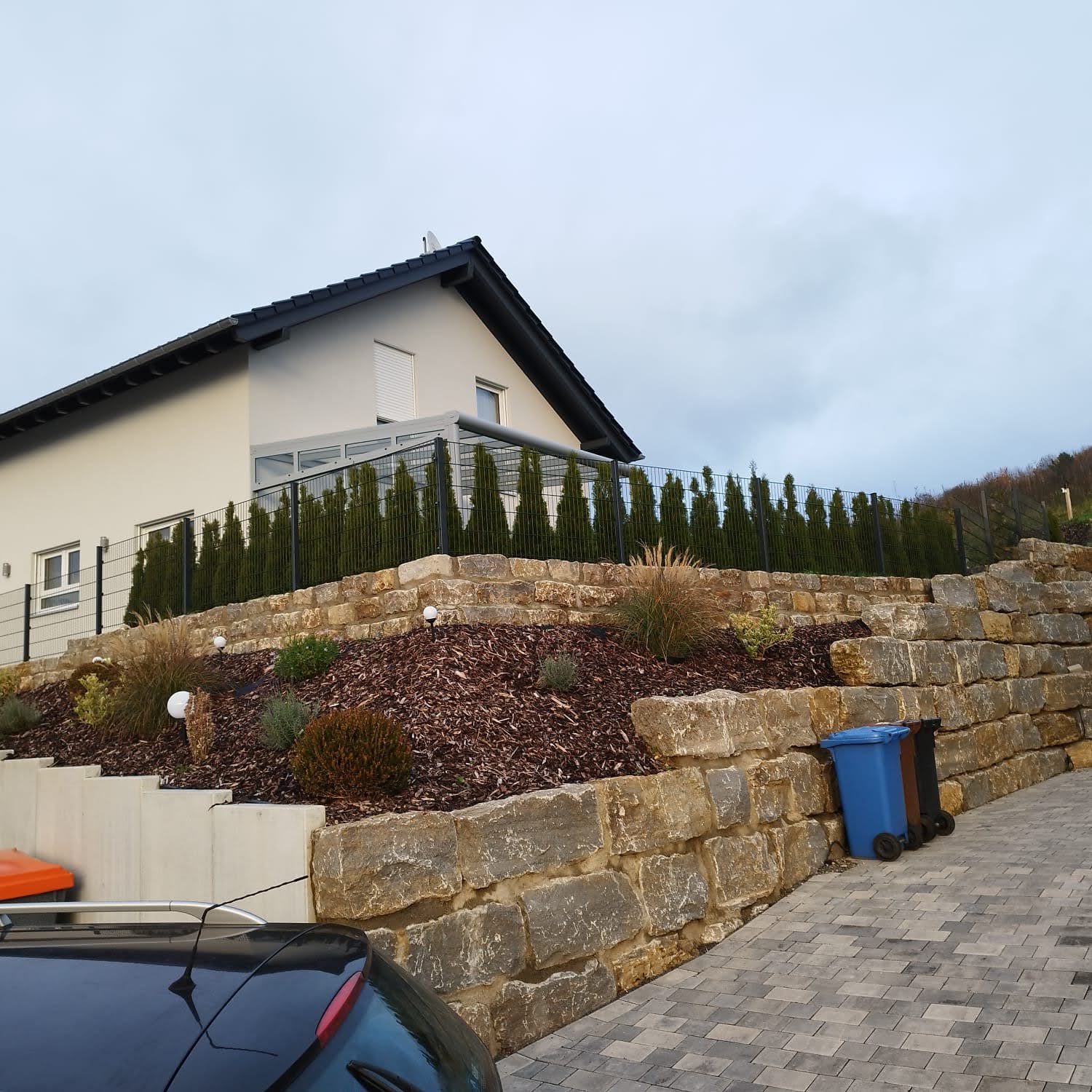 Gestaltete Außenanlage mit Natursteinmauer, Bepflanzung und Pflasterfläche durch Watan Gartenservice